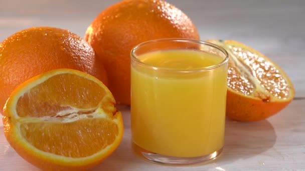 Várias baixas de suco que cai em um copo com o suco de laranja - movimento lento. Bebida alta e saborosa. Humor de verão. Sliced paz de laranja fresca na mesa. — Vídeo de Stock