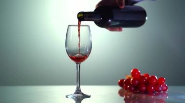 Kırmızı şarap güzel bir dalga oluşturur. Beyaz arka plandan şarap kadehi dökülüyor. Yakın plan çekim. Kırmızı şarabı kadehten kadehe yavaş yavaş dök..