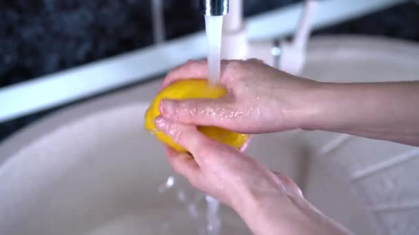 レモンを水で洗う。スローモーション。男の手は黄色のレモンを保持し、灰色の背景に水流の下でそれを洗う. — ストック動画