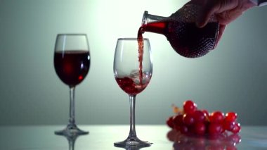 Kırmızı ve pembe arka planda şarap kadehleri dökülüyor. Kırmızı şarap güzel bir dalga oluşturur. Kırmızı şarabı şişeden cama yavaşça dökme hareketi. Yakın çekim..