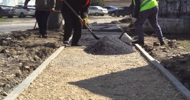Tým dělníků postavil horký asfalt na ulici podél tramvajových linek. Malý parní válec. Silniční dělníci s lopatami v ochranných uniformách. Práce v horkém dni. — Stock video