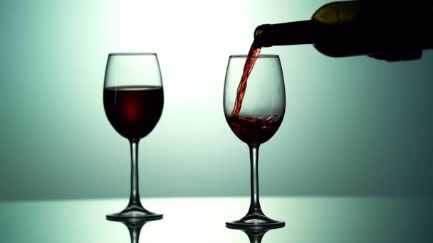 Víno nalévání ve sklenici vína na červeném a růžovém pozadí. Červené víno vytváří krásnou vlnu. Zpomalený pohyb nalévání červeného vína z láhve do skla. Záběr zblízka. 4k — Stock video
