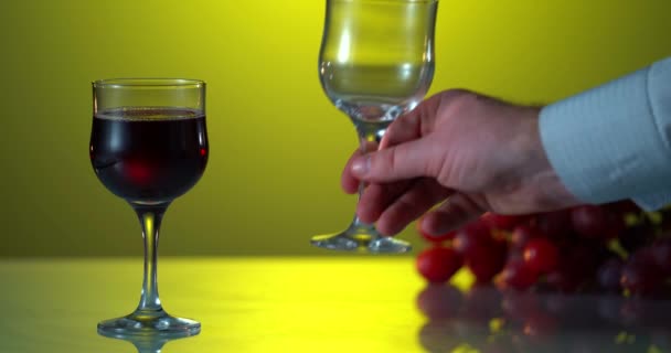 Advertising shot. Red wine from a bottle pours into a glass on a black background. Close up. Yellow background. Reflected table. Man put second glass on the surface — Stock Video