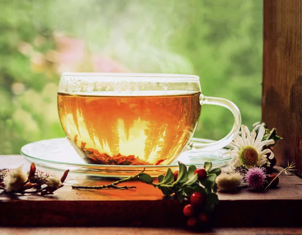 Une tasse de thé chaud sur un rebord de fenêtre parmi les herbes . — Photo
