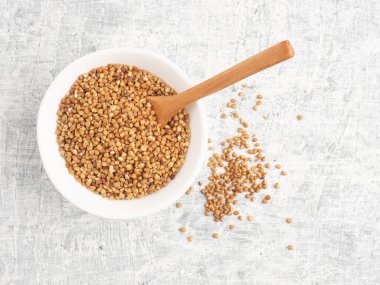 Beyaz seramik bir fincanda karabuğday ve beyaz bir arka planda tahta kaşık. Diyet ve kilo verme konsepti. Üst görünüm