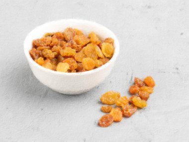 Beyaz bir fincanda kuru üzümler ve gri bir zemine serpilmiş, beton bir duvarda boyayla boyanmış. Yumuşak odak