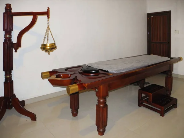 Beyaz duvara karşı tedavi odasında Ayurvedic masaj masası ve shirodhara cihazı. Kochi, Kerala, Hindistan. Ayurvedic sağlık kavramı