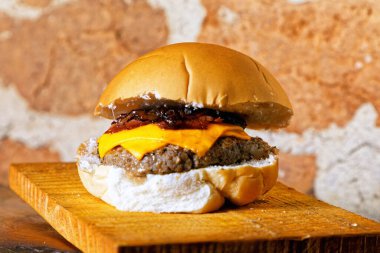 Hamburgerli nefis bir el yapımı sandviç, duble sarı peynir, ahşap tahtanın altında karamelli kızarmış soğan,
