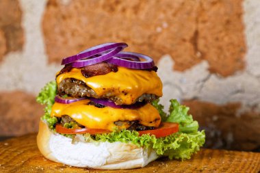 Yumurtalı lezzetli burger sandviç, domates peyniri, pastırma ve marul ahşap tahtanın altında kırsal duvarda arka planda.