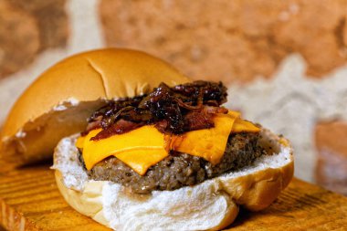 Hamburgerli nefis bir el yapımı sandviç, duble sarı peynir, ahşap tahtanın altında karamelli kızarmış soğan,