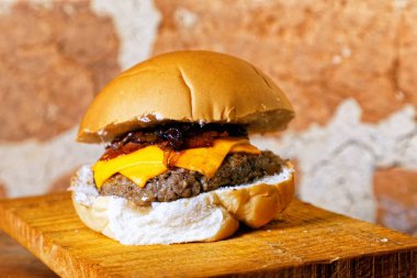 Hamburgerli nefis bir el yapımı sandviç, duble sarı peynir, ahşap tahtanın altında karamelli kızarmış soğan,