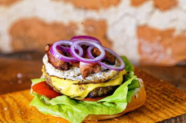 Yumurtalı lezzetli burger sandviç, domates peyniri, pastırma ve marul ahşap tahtanın altında kırsal duvarda arka planda.