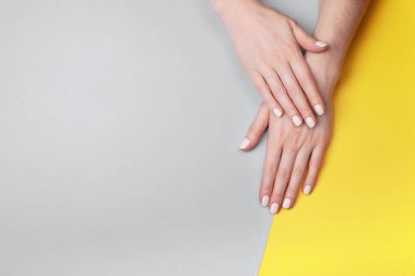 Gri-sarı arka planda klasik bir mat manikürü olan güzel kadın elleri.