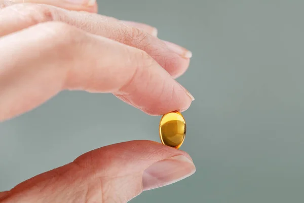 Weibliche Hand mit einer kleinen gelben Kapsel Nahrungsergänzungsmittel. Nahrungsergänzungsmittel, Vitamin D, Omega, Vitamin C. — Stockfoto