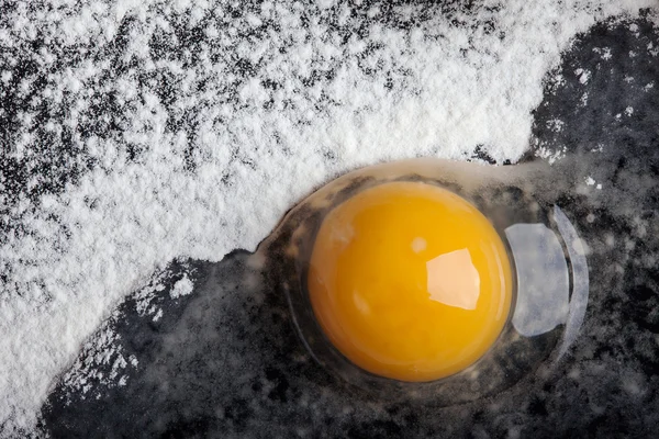 Złamane jaj na warstwie mąki na czarnym tle Zdjęcia Stockowe bez tantiem