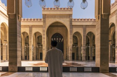 Bahreyn 'deki El Fetih Büyük Camii' nin güneş ışığıyla aydınlatılmış Kemerleri ve Dekoratif İslami Kaligrafi önünde bir dua.