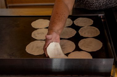 Geleneksel Meksikalı kadın eli sıcak ızgaraya taze mısır tortillası yerleştiriyor..