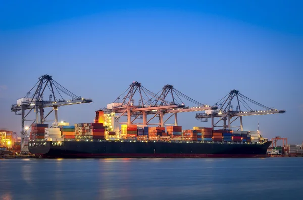 Cargo ship and crane at port reflect on river, twilight time — Stock Photo, Image