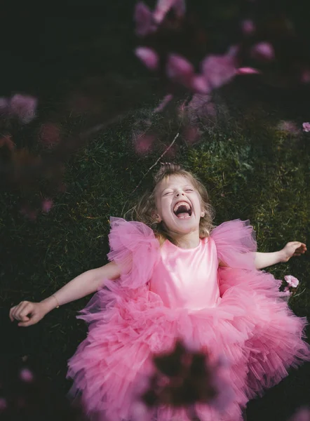 Šťastná dívka leží na zelené trávě v třešňovém květovém háji. — Stock fotografie