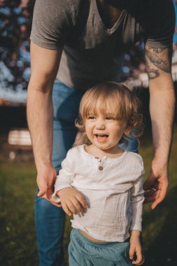 Bir baba, yürümeyi öğrenen çocuğuna destek olur..