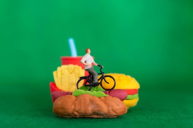 Minyatür insanlar fast food 'da bisiklet sürüyor, sağlıksız beslenme konsepti var.