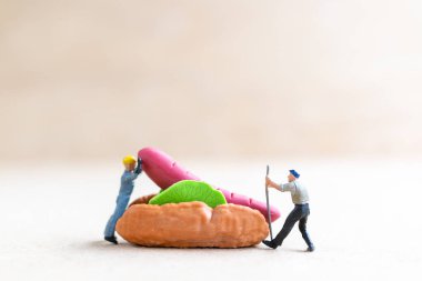 Miniature people workers make hot dog buns, fast food and junk food concept.