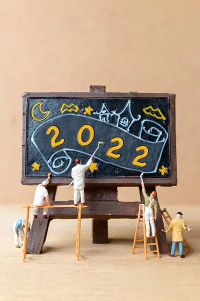 Miniature people worker team painting number 2022 on black board, Happy new year concept
