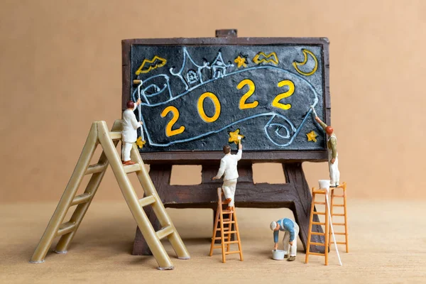 Miniature people worker team painting number 2022 on black board, Happy new year concept