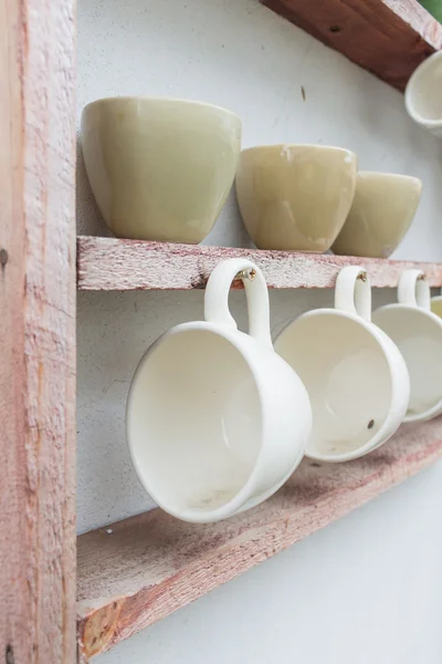 White coffee cup hanging on wooden shelf — Stock Photo, Image
