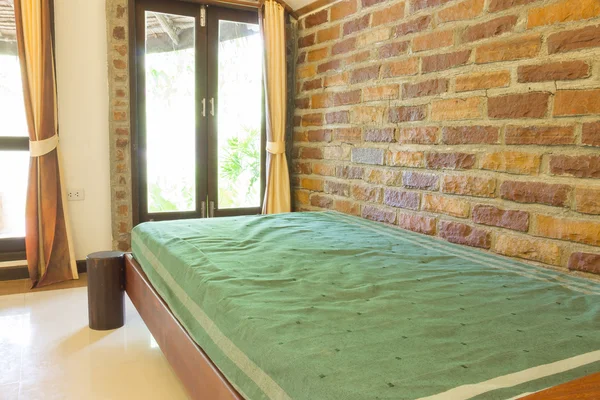 Een single bed naast bakstenen muur achtergrond — Stockfoto