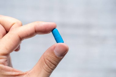 Parmaklar, eczacılık ve sağlık hizmetleri konsepti arasında mavi bir kapsülü tutan bir elin yakın çekimi