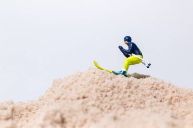 Beyaz arkaplanlı kum yüzeyinde kayak yapan minyatür kayakçı figürü, kopya alanı ile yaratıcı spor kavramı.