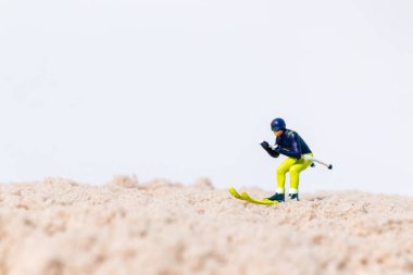 Beyaz arkaplanlı kum yüzeyinde kayak yapan minyatür kayakçı figürü, kopya alanı ile yaratıcı spor kavramı.