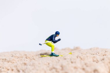 Beyaz arkaplanlı kum yüzeyinde kayak yapan minyatür kayakçı figürü, kopya alanı ile yaratıcı spor kavramı.