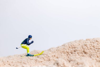 Beyaz arkaplanlı kum yüzeyinde kayak yapan minyatür kayakçı figürü, kopya alanı ile yaratıcı spor kavramı.