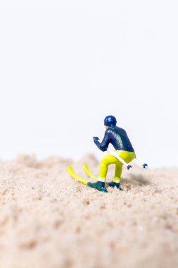 Beyaz arkaplanlı kum yüzeyinde kayak yapan minyatür kayakçı figürü, kopya alanı ile yaratıcı spor kavramı.