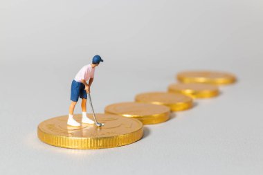 Yığılmış altın paraların üzerinde duran minyatür golfçü biblosu