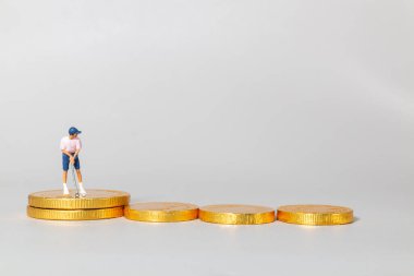 Yığılmış altın paraların üzerinde duran minyatür golfçü biblosu