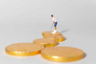 Yığılmış altın paraların üzerinde duran minyatür golfçü biblosu