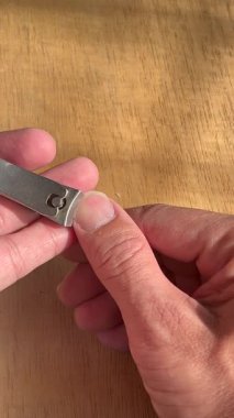 Ellerin tırnaklarını paslanmaz çelik tırnak makasıyla doğal güneş ışığında tahta bir yüzey üzerinde kestiği dikey makro video..