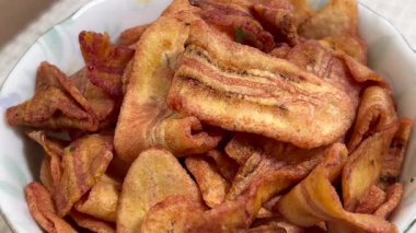 Seramik bir kasede kıtır kıtır kızarmış muz dilimlerinin yakın çekim görüntüleri, yavaş yavaş vitrinlere, çıtır çıtır dokulara ve lezzetli Tayland sokak atıştırmalıklarına dönüşüyor..