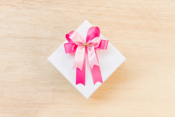 Arco de cinta rosa y caja de regalo blanca sobre fondo de madera — Foto de Stock