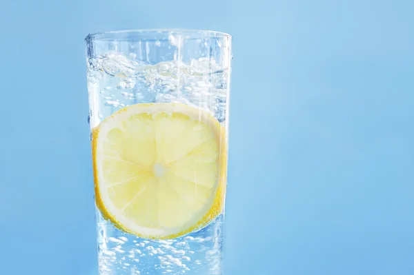 fresh cool water with lemon in glass on natural blue wooden backround