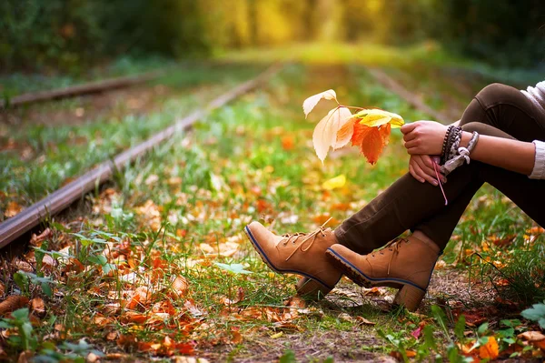 Kobieta siedzi na szlakach kolejowych i przytrzymując kolorowych liści jesienią — Zdjęcie stockowe