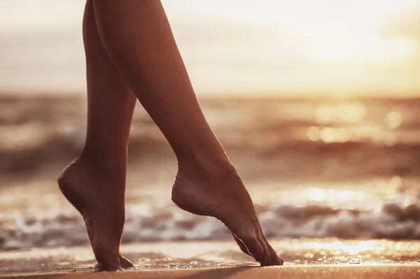Gambe di donna sexy sulla spiaggia di sabbia con acqua di mare e tramonto — Foto Stock