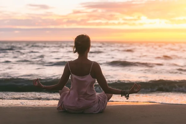 Молодая женщина практикует йогу на песчаном пляже океана на закате — стоковое фото