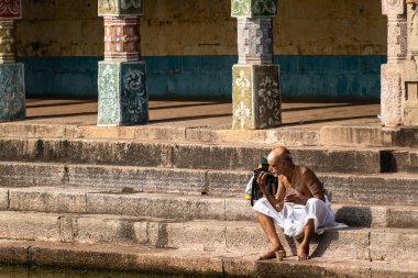 Mayiladuthurai, Tamil Nadu, Hindistan - Şubat 2020: Vaitheeswaran Koil 'deki antik Hindu tapınağının içindeki kutsal bir tankın taş basamaklarında oturan yaşlı bir Hintli rahip.