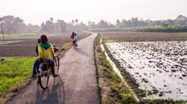 Murshidabad, Batı Bengal, Hindistan - Ocak 2018: Çocuklar Murshidabad ilçesinde yeşil alanlardan geçen dar bir kırsal yolda bisiklet sürüyorlar,