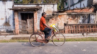 Murshidabad, Batı Bengal, Hindistan - Ocak 2018: Eski Murshidabad kasabasında bir kır evinin önünden bisikletle geçen Hintli bir adam.