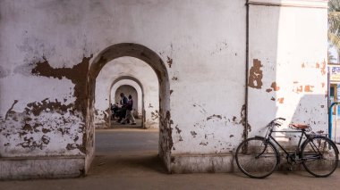 Murshidabad, Batı Bengal, Hindistan - Ocak 2018: Murshidabad kasabasında perspektifi azalan eski, kemerli, solgun bir tünelin duvarlarının yanına park edilmiş bir bisiklet.